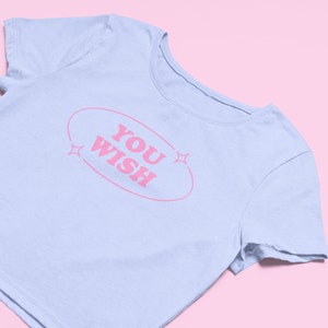 May include: A light blue cropped t-shirt with a pink oval graphic that says "YOU WISH" with pink stars on either side.