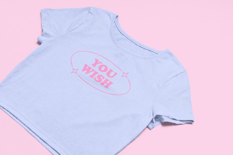 May include: A light blue cropped t-shirt with a pink oval graphic that says "YOU WISH" with pink stars on either side.
