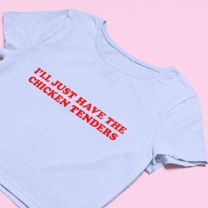 May include: A light blue cropped t-shirt with red text that reads "I'll just have the chicken tenders".