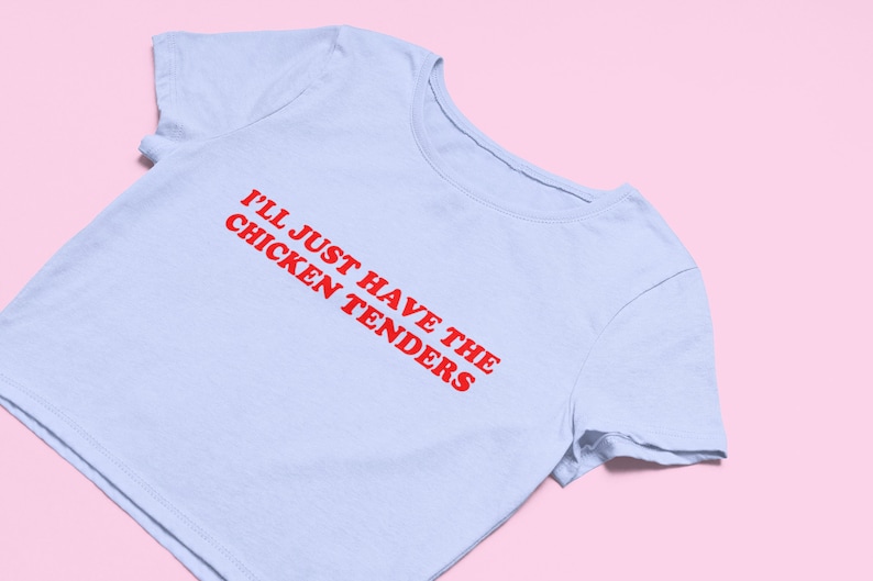 May include: A light blue cropped t-shirt with red text that reads "I'll just have the chicken tenders".