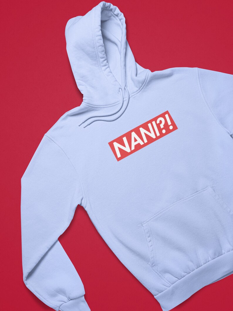 K&ouml;nnte beinhalten: Hellblauer Kapuzenpullover mit Fronttasche und Kordelzugkapuze. Auf der Vorderseite des Hoodies steht das Wort "NANI?!" in wei&szlig;er Schrift in einem roten Rechteck.