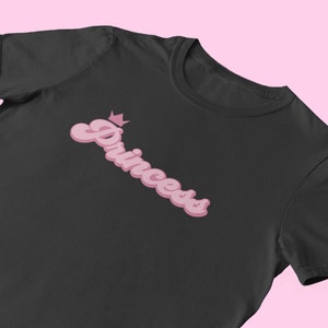 May include: Black t-shirt with a pink retro-style graphic that says "Princess" with a crown above the word.