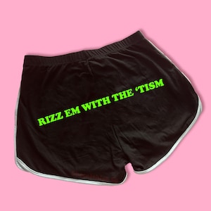 May include: Black athletic shorts with a white trim and the text "Rizz Em With The Tism" in green.