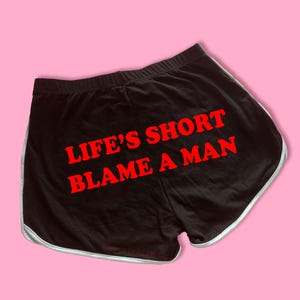 May include: Black athletic shorts with white trim and the text "LIFE'S SHORT BLAME A MAN" in red.
