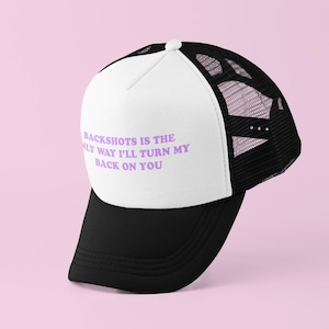May include: A black and white trucker hat with the text "Backshots is the only way I'll turn my back on you" in purple. The hat has a white front panel and a black mesh back, with a black brim.