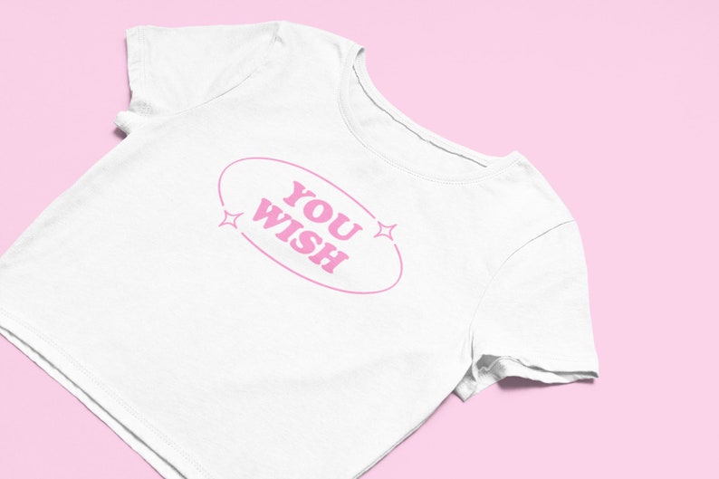 May include: White crop top with pink text that reads "YOU WISH" inside an oval with two pink stars on either side.