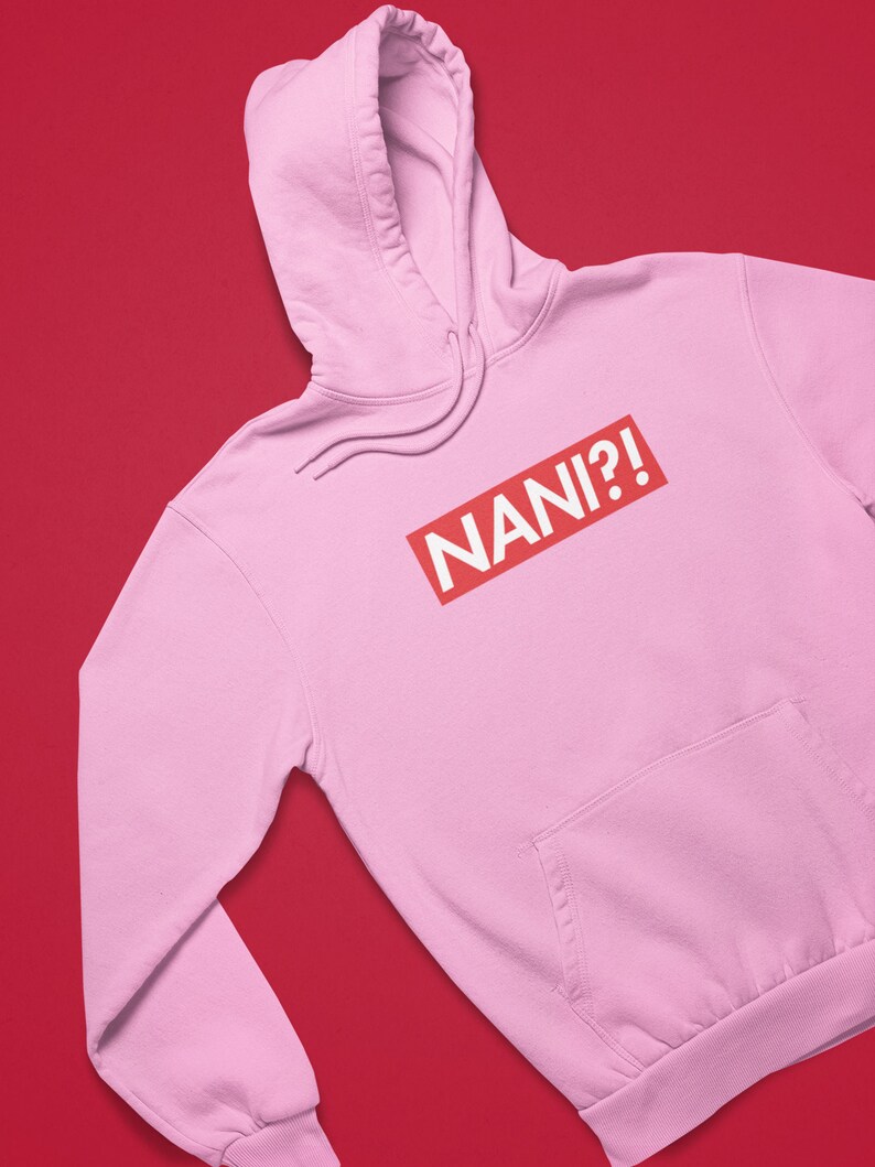 K&ouml;nnte beinhalten: Hellrosa Kapuzenpullover mit Kordelzug und Vordertasche. Der Schriftzug "NANI?!" ist in wei&szlig;en Buchstaben in einem roten Rechteck auf der Vorderseite aufgedruckt.
