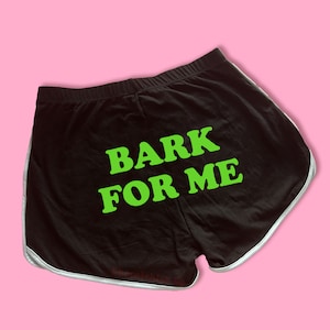 May include: Black athletic shorts with white trim and the text "BARK FOR ME" in green.