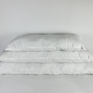 May include: Three white rectangular pillows stacked on top of each other. The pillows are made of a soft, fluffy material and are perfect for sleeping or lounging.