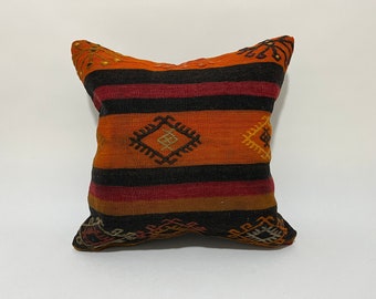 May include: A decorative pillow with a striped pattern in shades of orange, red, black, and brown. The pillow features a geometric design with a diamond shape in the center.