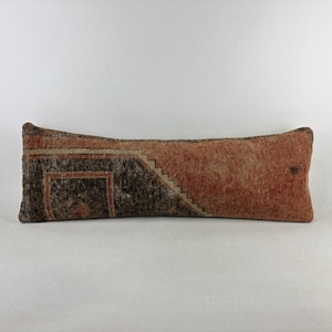 May include: A long, rectangular lumbar pillow featuring a textured, woven surface. The design is split diagonally, with one side in a deep charcoal black featuring a geometric border pattern and the other side in a muted, earthy terracotta orange.