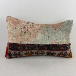 May include: A rectangular throw pillow featuring a two-tone design. The top section displays a faded, distressed floral pattern in muted peach and sage green. The bottom section features a dark charcoal band with geometric red and yellow motifs.