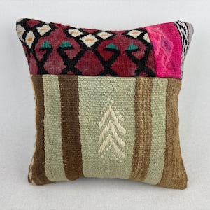 May include: A square throw pillow featuring a top section with a dark red, black, and white geometric pattern and a bright pink accent. The bottom section consists of light green and brown vertical stripes with a central white chevron design.