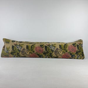 May include: A long, rectangular pillow with a floral pattern. The pillow features pink, green, and blue flowers on a beige background. The pillow is approximately 30 inches long.