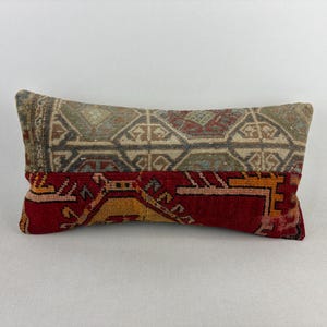 May include: A rectangular throw pillow featuring a two-tone design. The top half displays a muted, earth-toned geometric pattern in shades of beige, grey, and faded blue, while the bottom half features a vibrant red section with yellow and black motifs.