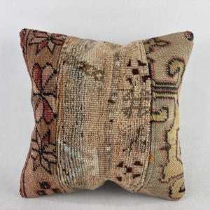 May include: Square decorative pillow with a patchwork design. The pillow features a mix of colors, including beige, brown, and red, with floral and geometric patterns. The pillow is made of a textured fabric.