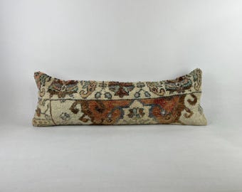 May include: A long, rectangular pillow with a cream-colored background and a colorful, intricate pattern. The pattern features shades of orange, red, blue, and green.