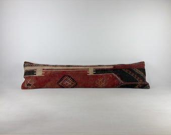 Peut inclure: Un long coussin lombaire rectangulaire doté d'une housse en textile tissé avec une couleur de base rouge profond. Le tissu présente des motifs géométriques complexes en noir, crème et brun foncé, incluant des losanges et des bordures linéaires.