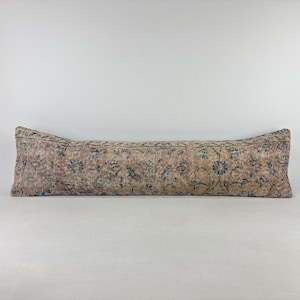 Puede incluir: Un cojín largo y rectangular con un aspecto vintage descolorido. Presenta un estampado floral en tonos rosa, azul y beige. El diseño recuerda a una alfombra tradicional, añadiendo un toque de encanto antiguo a la decoración del hogar. Mide unos 100 cm de largo.