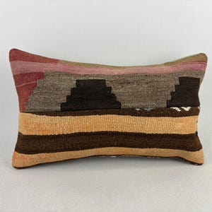 May include: A rectangular throw pillow featuring a woven textile cover with a horizontal design. The top section displays a dark brown geometric pattern against a muted mauve and tan background, while the bottom half consists of alternating horizontal stripes in shades of light tan and dark brown.