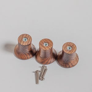 May include: Three wooden cabinet knobs with a rich, dark brown grain pattern. Each knob has a rounded base and a cylindrical top, with a silver screw visible in the center. Several silver screws are also present.