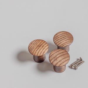 May include: Three wooden cabinet knobs with a rounded top and a dark brown base. The knobs have a natural wood grain pattern. Several silver screws are next to the knobs. The knobs are likely for furniture.
