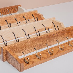 Può includere: Quattro attaccapanni in legno in varie tonalità di marrone e legno naturale. Ogni attaccapanni presenta più ganci per appendere oggetti. Gli attaccapanni sono esposti ad angolo, mostrando il loro design e la loro costruzione.