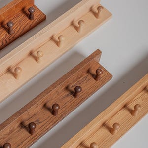 May include: Wooden coat racks in various shades of brown and tan. Each rack features multiple rounded pegs for hanging items. The racks are made of wood and have a simple, minimalist design. The racks are approximately 24 inches long.