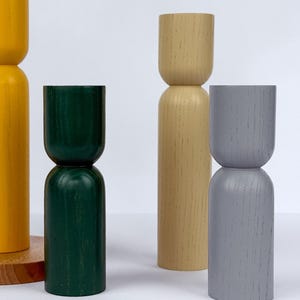 May include: Four wooden decorative objects in yellow, green, beige, and gray. The objects have a two-part design, with a rounded top and a cylindrical or rounded base. The yellow object is on a wooden base. The objects are on a white surface.