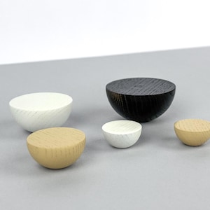 Może przedstawiać: Zestaw pięciu drewnianych misek w różnych rozmiarach i kolorach. Miski mają kształt półkul, z białym, czarnym i naturalnym wykończeniem drewna. Miski są ułożone na szarej powierzchni, prezentując ich unikalne tekstury i kształty.