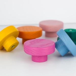 May include: A collection of colorful wooden mushroom-shaped knobs in various shades, including yellow, orange, pink, blue, and green. These decorative knobs are designed for furniture and add a vibrant touch to any room. The knobs are made of wood.
