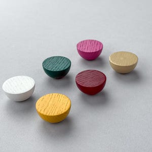 May include: Six colorful, half-sphere wooden knobs in a variety of colors: white, green, pink, red, yellow, and tan. Each knob has a textured, wood-grain surface. The knobs are arranged on a light gray background.