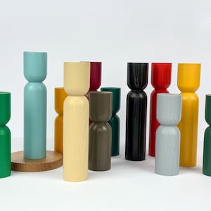 Puede incluir: Una colección de 11 candelabros de madera en varios colores, incluyendo verde, azul, amarillo, rojo, negro y gris. Los candelabros tienen todos la misma forma, con una base ancha y una parte superior estrecha.