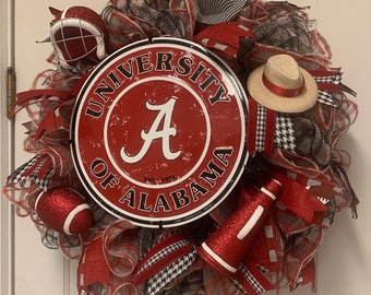 May include: A red, white, and black University of Alabama wreath with a red and white football, a red and white megaphone, a red and white hat, and a red and white football helmet.