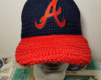 May include: A blue and red crocheted baseball cap with a red "A" logo on the front.