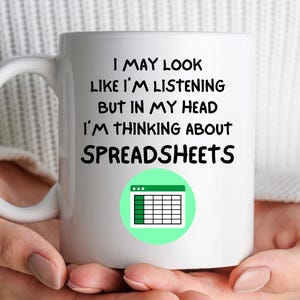 May include: White ceramic mug with the text "I MAY LOOK LIKE I'M LISTENING BUT IN MY HEAD I'M THINKING ABOUT SPREADSHEETS". The mug also features a green circle with a spreadsheet icon.