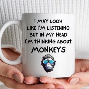 May include: White ceramic coffee mug with a black and white illustration of a monkey wearing sunglasses. The text on the mug reads "I may look like I'm listening but in my head I'm thinking about monkeys."