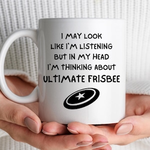May include: White ceramic mug with a black and white graphic of a frisbee and the text: "I MAY LOOK LIKE I'M LISTENING BUT IN MY HEAD I'M THINKING ABOUT ULTIMATE FRISBEE."
