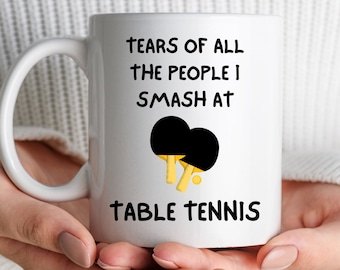 May include: White ceramic coffee mug with a black and yellow table tennis paddle graphic and the text "Tears of all the people I smash at table tennis".