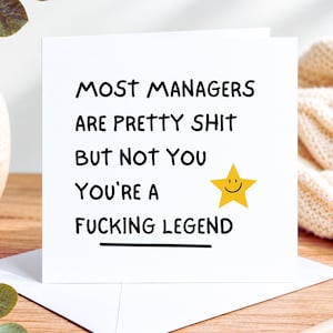 May include: A square white greeting card with black text that reads: MOST MANAGERS ARE PRETTY SHIT BUT NOT YOU YOU'RE A FUCKING LEGEND. A yellow five-pointed star with a simple black smiley face is printed next to the text on the card.