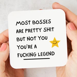 May include: A white square card with rounded corners, held by hands with pink nail polish. The card features black text that reads "MOST BOSSES ARE PRETTY SHIT BUT NOT YOU YOU'RE A FUCKING LEGEND" with a yellow star.