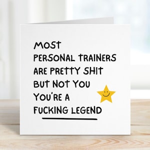 May include: A white greeting card with black text that reads "MOST PERSONAL TRAINERS ARE PRETTY SHIT BUT NOT YOU YOU'RE A FUCKING LEGEND." A yellow star with a smiling face is to the right of the text.