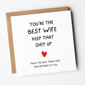 以下が含まれることがあります： 黒い文字で「YOU'RE THE BEST WIFE KEEP THAT SHIT UP」と書かれた正方形の白いグリーティングカード。テキストの下には小さな赤いハートがあり、その下に「FROM THE BEST THING THAT EVER HAPPENED TO YOU」と書かれています。カードは茶色の封筒の上に置かれています。