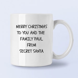 Op de afbeelding: Witte keramische mok met zwarte tekst die luidt: "Merry Christmas to you and the family Paul. From Secret Santa."