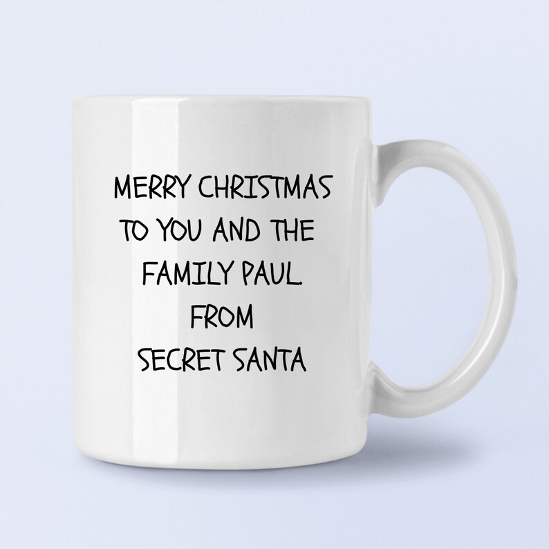 Op de afbeelding: Witte keramische mok met zwarte tekst die luidt: "Merry Christmas to you and the family Paul. From Secret Santa."