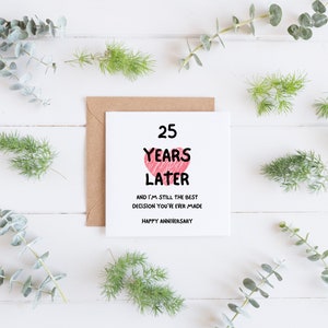 Op de afbeelding: Een witte kaart met een roze hart en de tekst "25 Years Later and I'm still the best decision you've ever made. Happy Anniversary."