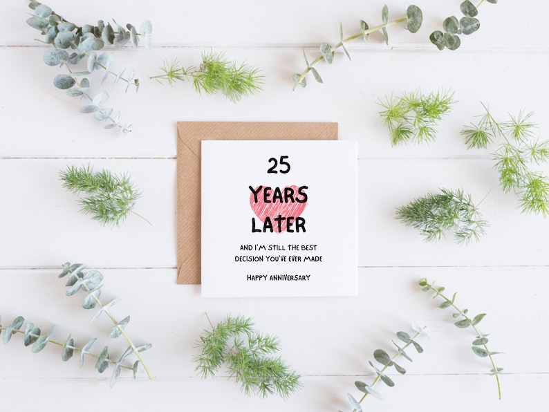 Op de afbeelding: Een witte kaart met een roze hart en de tekst "25 Years Later and I'm still the best decision you've ever made. Happy Anniversary."