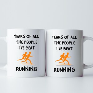 K&ouml;nnte beinhalten: Zwei wei&szlig;e Keramikbecher mit schwarzem Text, der "TEARS OF ALL THE PEOPLE I'VE BEAT" und "RUNNING" lautet. Jeder Becher zeigt eine orangefarbene Grafik von zwei L&auml;ufern.