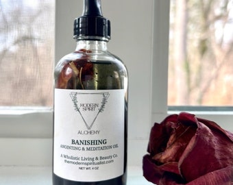 May include: A glass bottle with a black dropper top filled with a dark liquid and dried rose petals. The label reads "ALCHEMY BANISHING ANOINTING & MEDITATION OIL A Wholistic Living & Beauty Co. themodernspiritualist.com NET WT. 4 OZ"