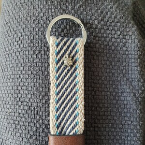 Peut inclure: Un porte-cl&eacute;s tiss&eacute; avec un motif ray&eacute; cr&egrave;me, marine et bleu clair. Il est orn&eacute; d'un petit charm en forme de tortue argent&eacute;e, d'une bande en cuir marron et d'un porte-cl&eacute;s argent&eacute;.